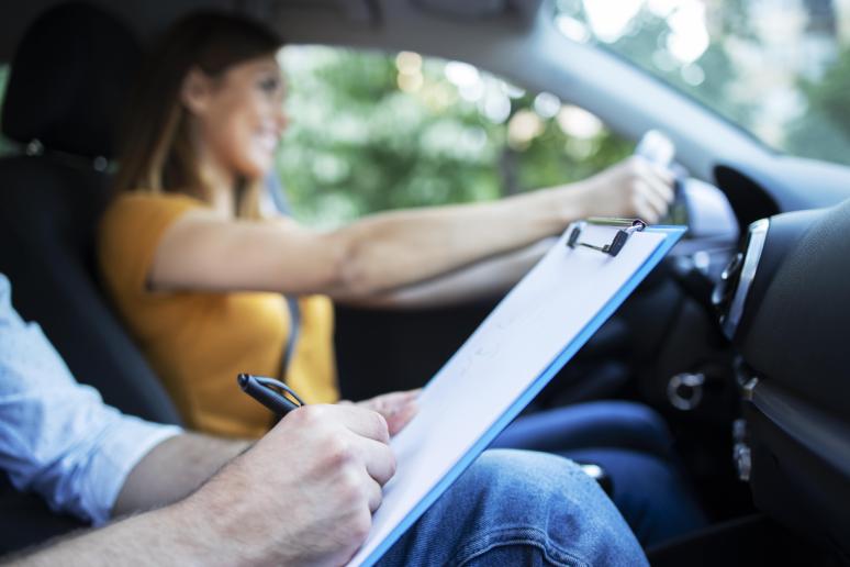 close up view driving instructor holding checklist while background female student steering driving car